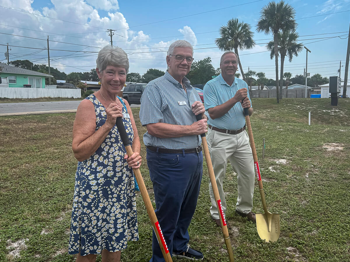 Three people hold shovels on the church lawn.