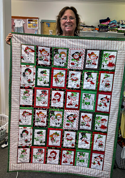 Quilter displays a newly made quilt in a Christmas theme.