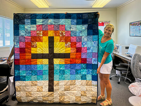 Quilter displays a newly made quilt with a beautiful cross on it.
