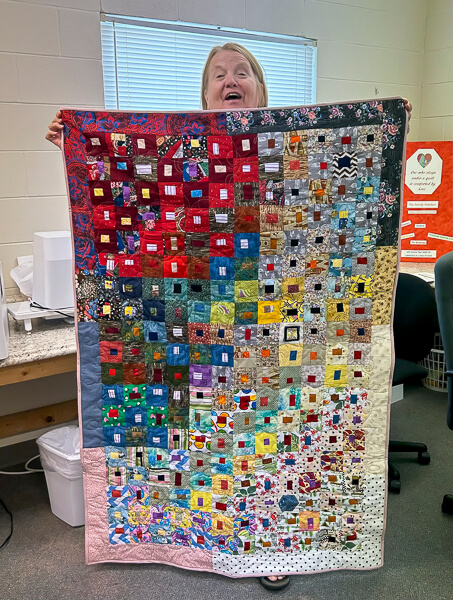 Woman holds newly sewn quilt.