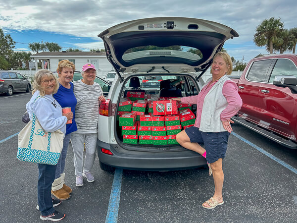 Four women stand around a car with Operation Christmas Child boxes in the trunk.