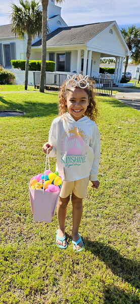 A young girl smiles while holding a large bag of Easter eggs.