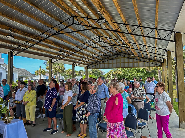 Worshippers gather outdoors in pavilion.