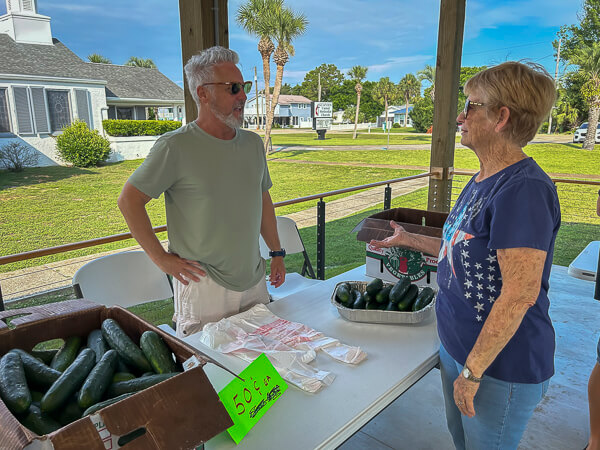 Two people chat at the table with produce being sold