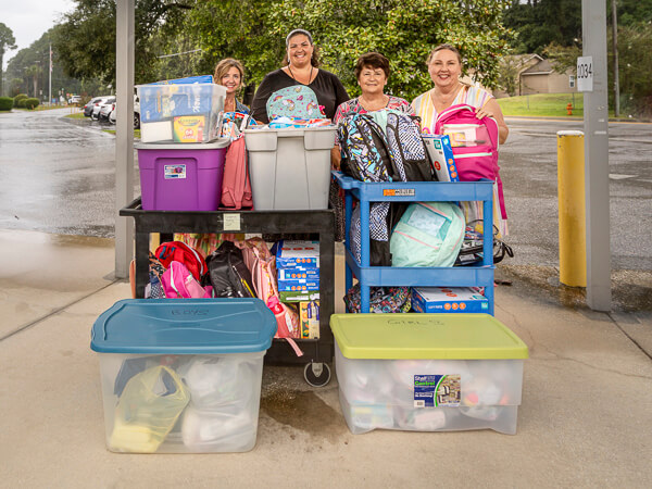 Women stand behind large stacks of donations.