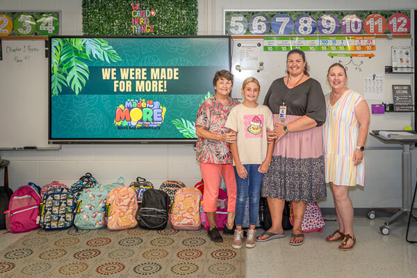 Teacher, student, and Gulfview members stand beside donated backpacks in the teacher's classroom.