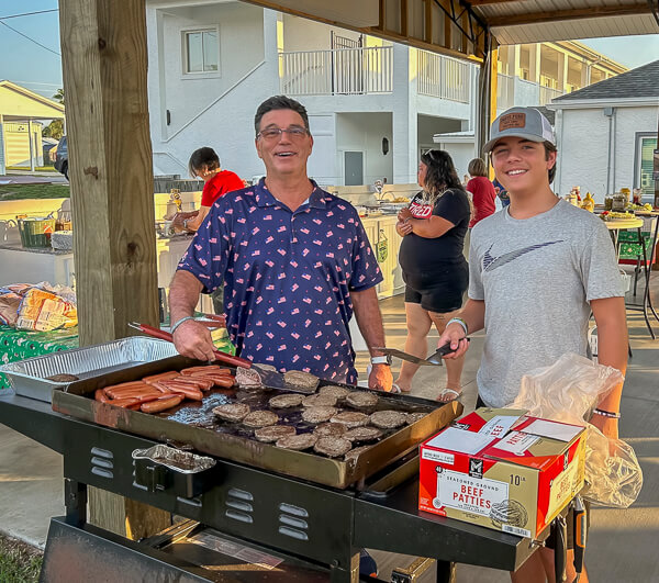 Two men grill burgers and hot dogs.