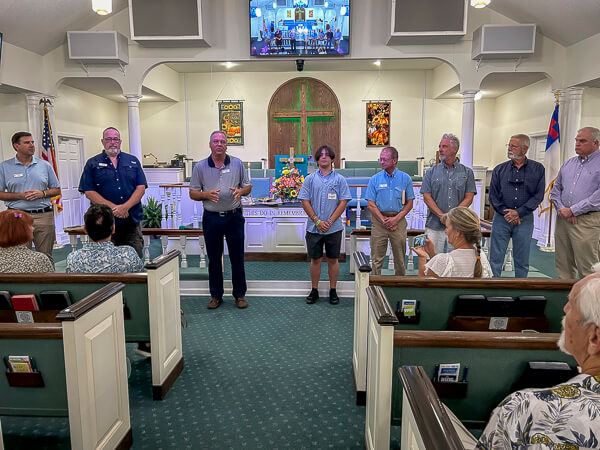 Pastor and seven men stand at the front of the sanctuary