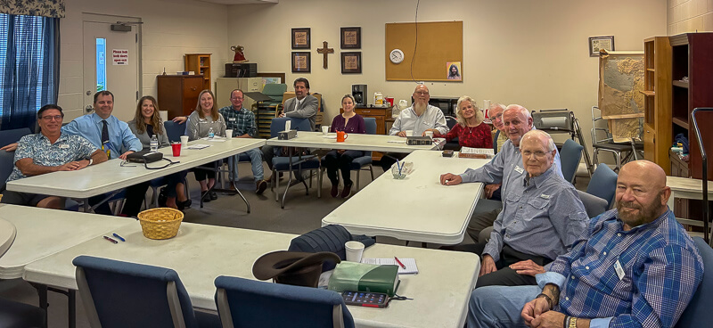 Group of adults sits at tables in Sunday School classroom.