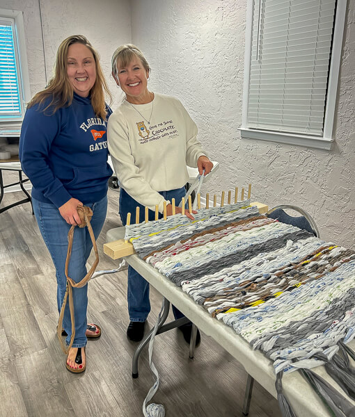 Two women work on making mats from plastic grocery bags.