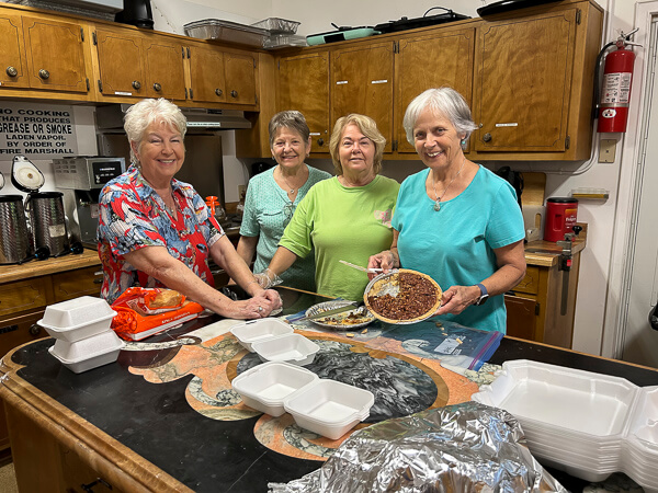 Four women prepare food in the church kitchen.