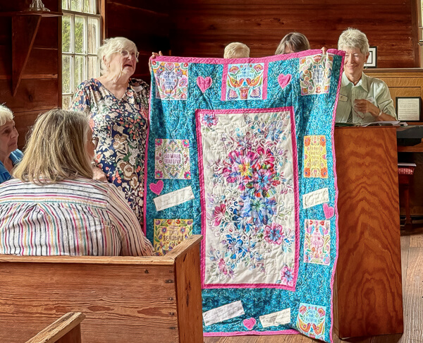 Woman happily accepts the gift of a quilt made by the Seaside Stichers