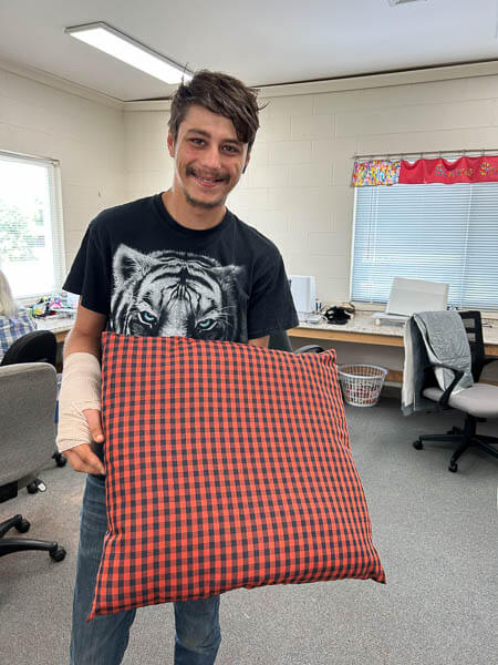 Man holds completed pillow in sewing room.