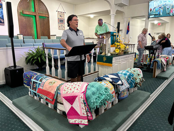 Quilts are displayed in the pulpit area as people sing.