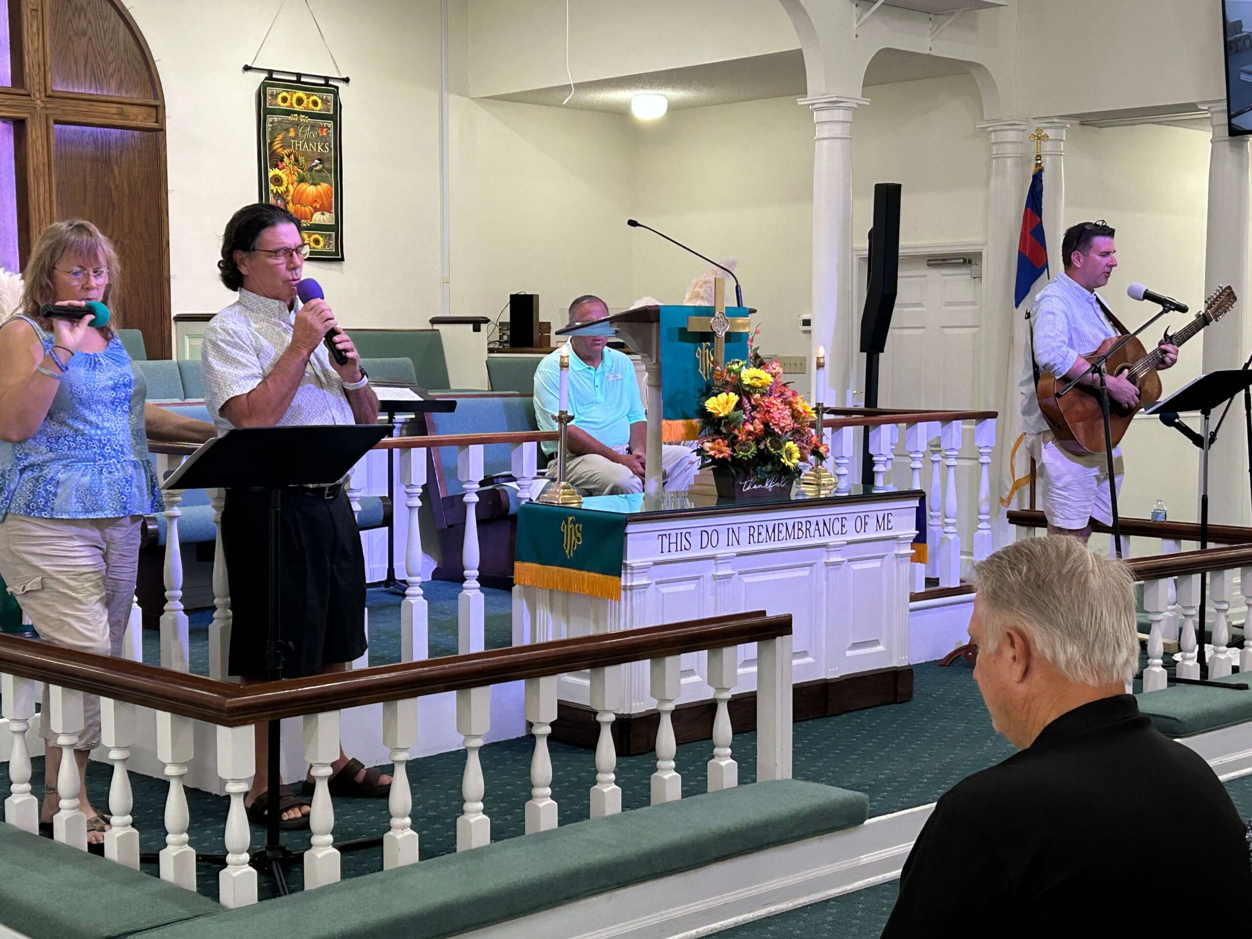 Man plays guitar and two others sing during worship service.
