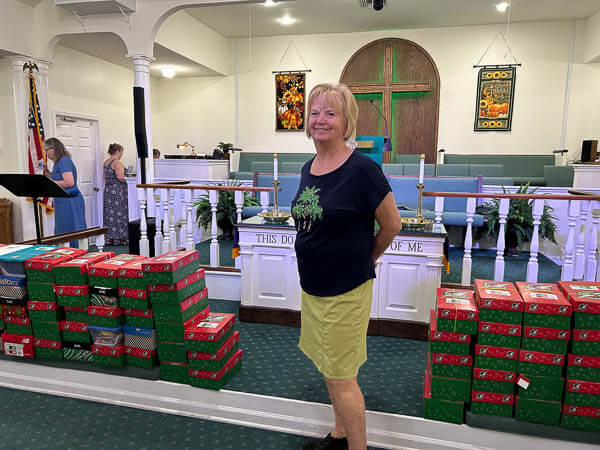 Woman poses in front of Operation Christmas Child boxes