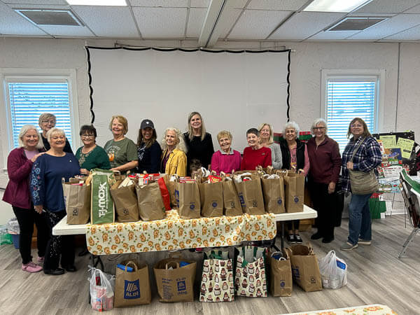Women gather behind a table of bags of Thanksgiving food donations.