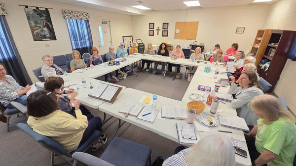 Ladies gather in a room around tables for Bible Study