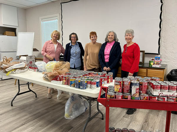 Ladies stand behind table of canned soup