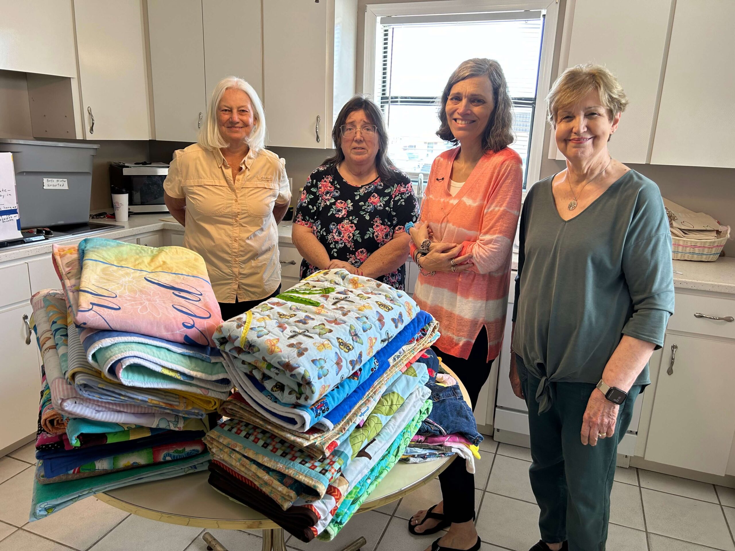 Four women stand behind a stack of baby quilts.