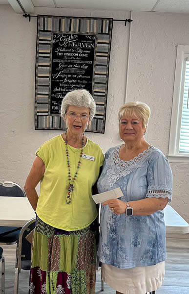 Woman hands a check to another woman.